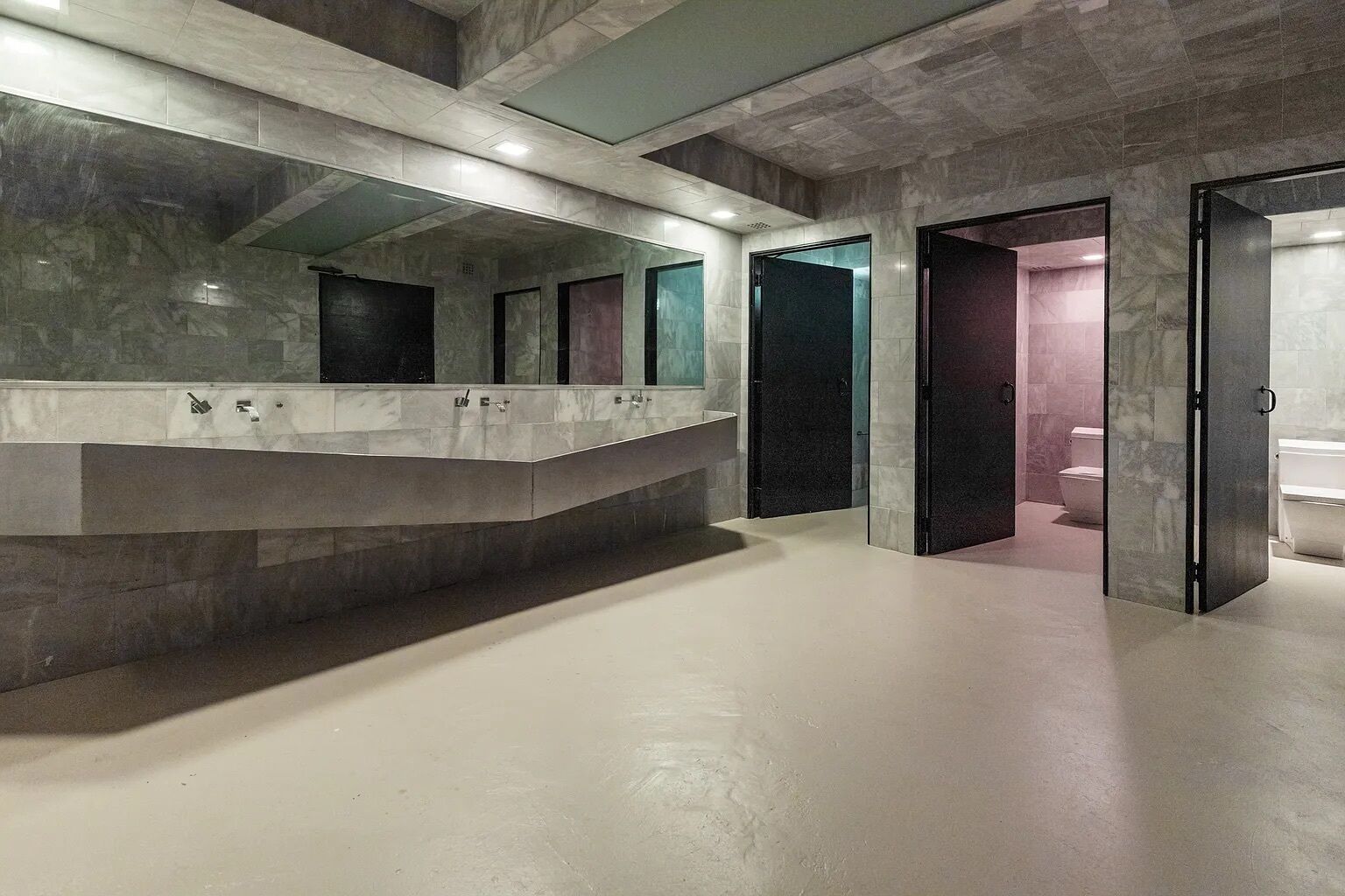 A modern bathroom with marble countertops, a large mirror, and a toilet visible through a glass door.