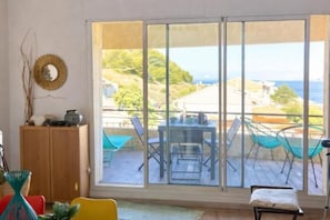 A room with a large sliding glass door leading to an outdoor deck with a table and chairs. - T3 Duplex Cosy with Terrace and Sea View - 5 min from the Beach (Marseille)