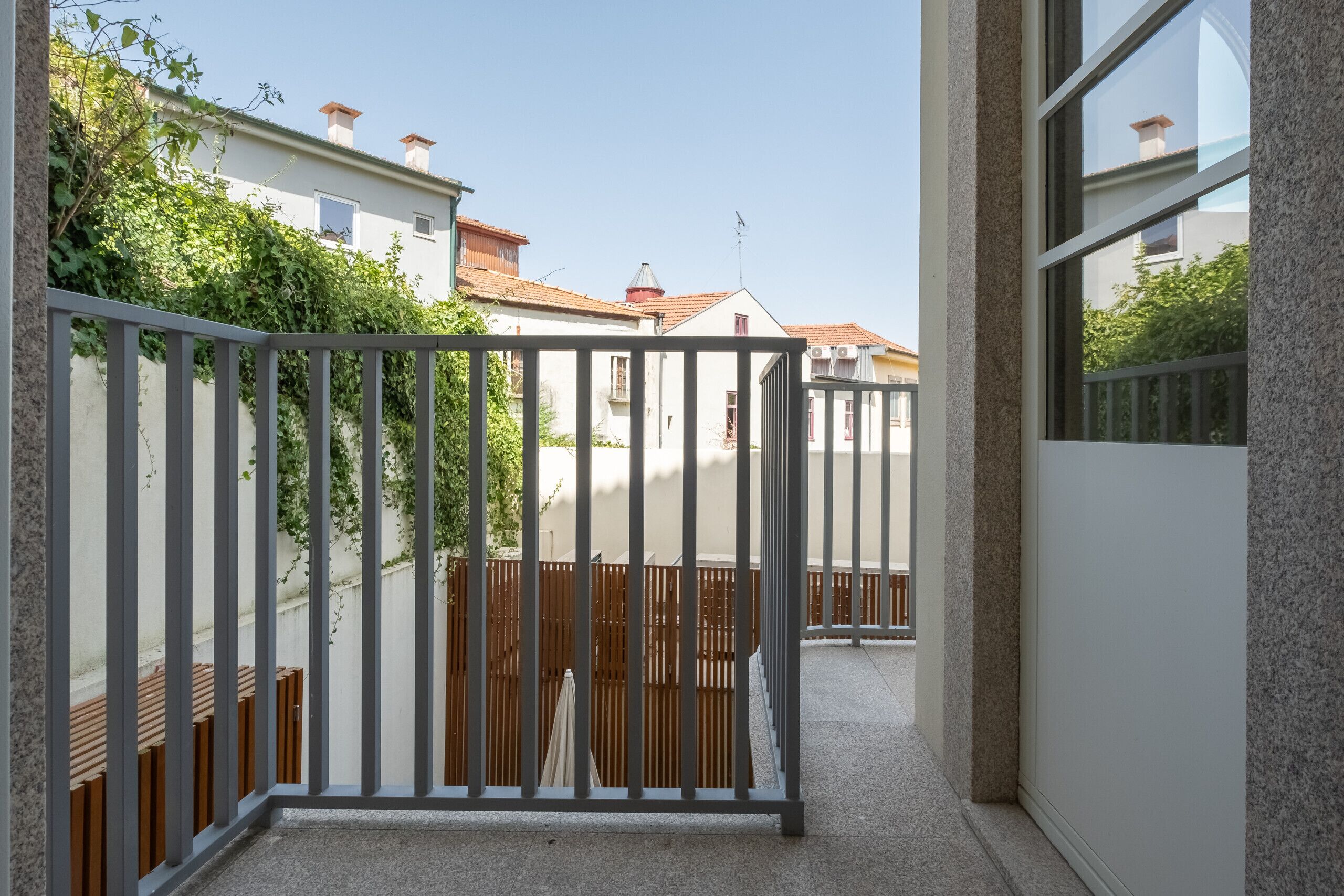 Un pasillo estrecho con una reja metálica, cerca de madera y vistas de edificios vecinos.