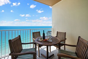 A balcony with a view of the ocean, a round wooden table with chairs, and a bottle of wine. - Newly Updated Gulf Front 2-Bedroom Condo; Direct Ocean Views in Gulf Shores, AL (Gulf Shores)