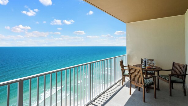 A balcony with a view of the ocean, a table with chairs, and a bottle of wine. - Newly Updated Gulf Front 2-Bedroom Condo; Direct Ocean Views in Gulf Shores, AL (Gulf Shores)