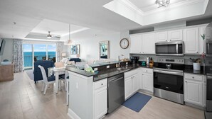 A modern kitchen with white cabinets, stainless steel appliances, and a dining area with a view. - Newly Updated Gulf Front 2-Bedroom Condo; Direct Ocean Views in Gulf Shores, AL (Gulf Shores)