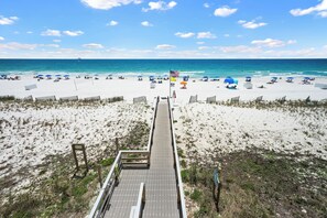 A beach with a wooden boardwalk leading to the water, a flag, and beach umbrellas. - Newly Updated Gulf Front 2-Bedroom Condo; Direct Ocean Views in Gulf Shores, AL (Gulf Shores)