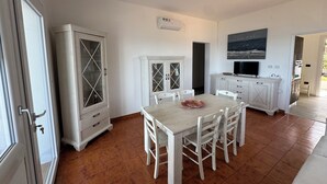 Un comedor con una mesa y sillas, un mueble con puertas de cristal, un televisor y un cuadro en la pared.