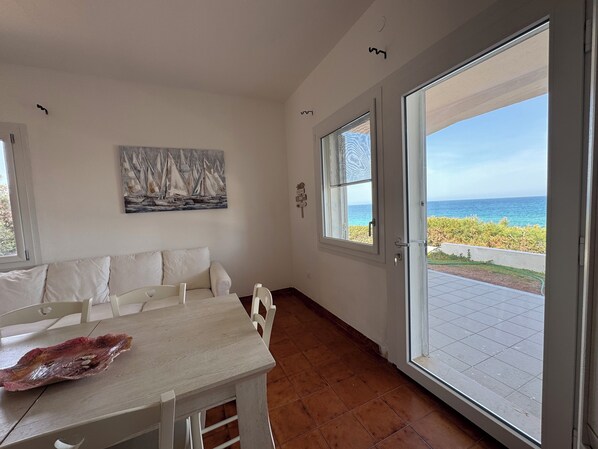 Une pièce comprenant une table à manger et des chaises, un tableau accroché au mur et une grande fenêtre donnant sur la mer.