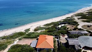 Vista aérea de una propiedad costera con playa, una casa de techo rojo y paneles solares.