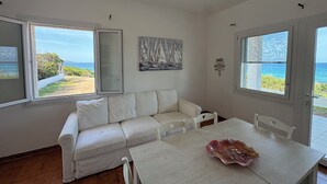 Una habitación con un sofá blanco, una mesa de comedor y vista a la playa.