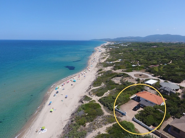 An aerial view of a beach with a clear blue sea, a sandy shore lined with umbrellas, and a building circled in yellow. - Beachfront Villa - Stunning Ocean View (Maragnanu)