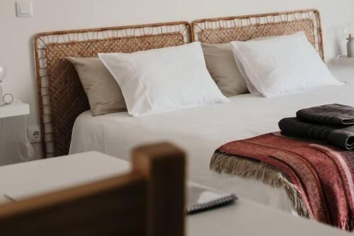 Ein Bett mit einem gewobenen Kopfteil, einem runden Spiegel an der Wand und einer roten Tagesdecke.