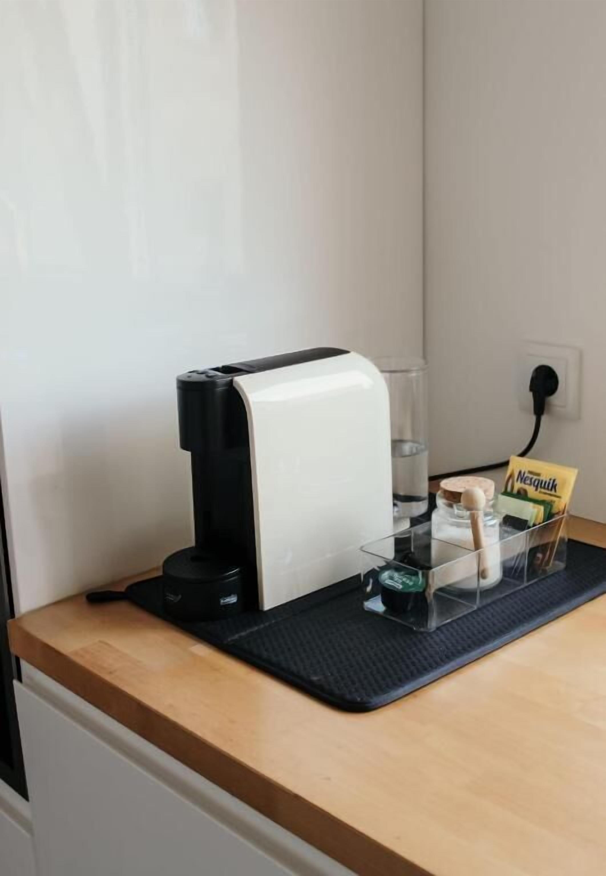 Eine Kaffeemaschine auf einer Arbeitsplatte mit einer transparenten Glaskanne, einer Kaffeecréme-Glase und einer Packung Nespresso-Kapseln.