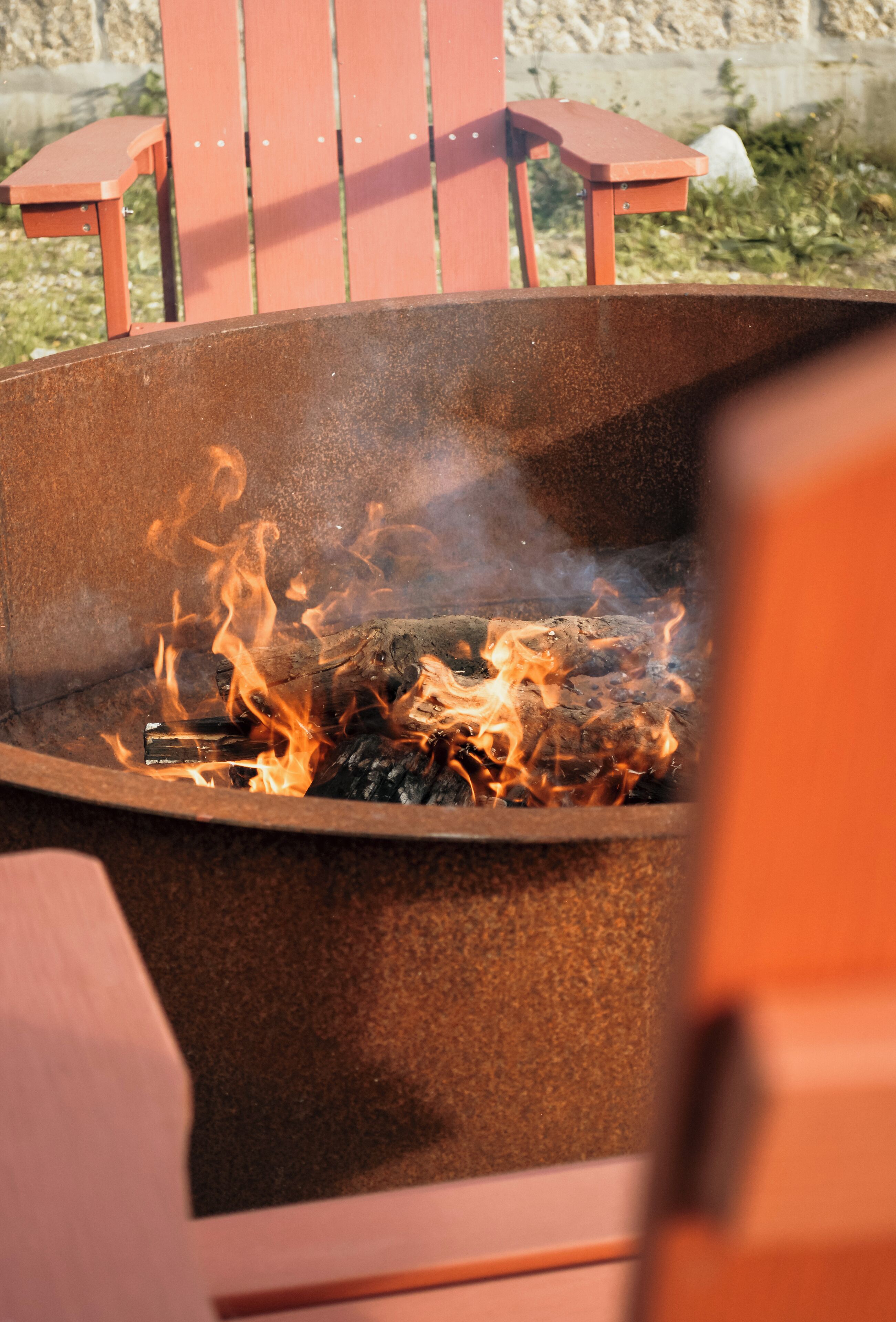 A metal fire pit with burning logs and flames, surrounded by a red wooden structure.