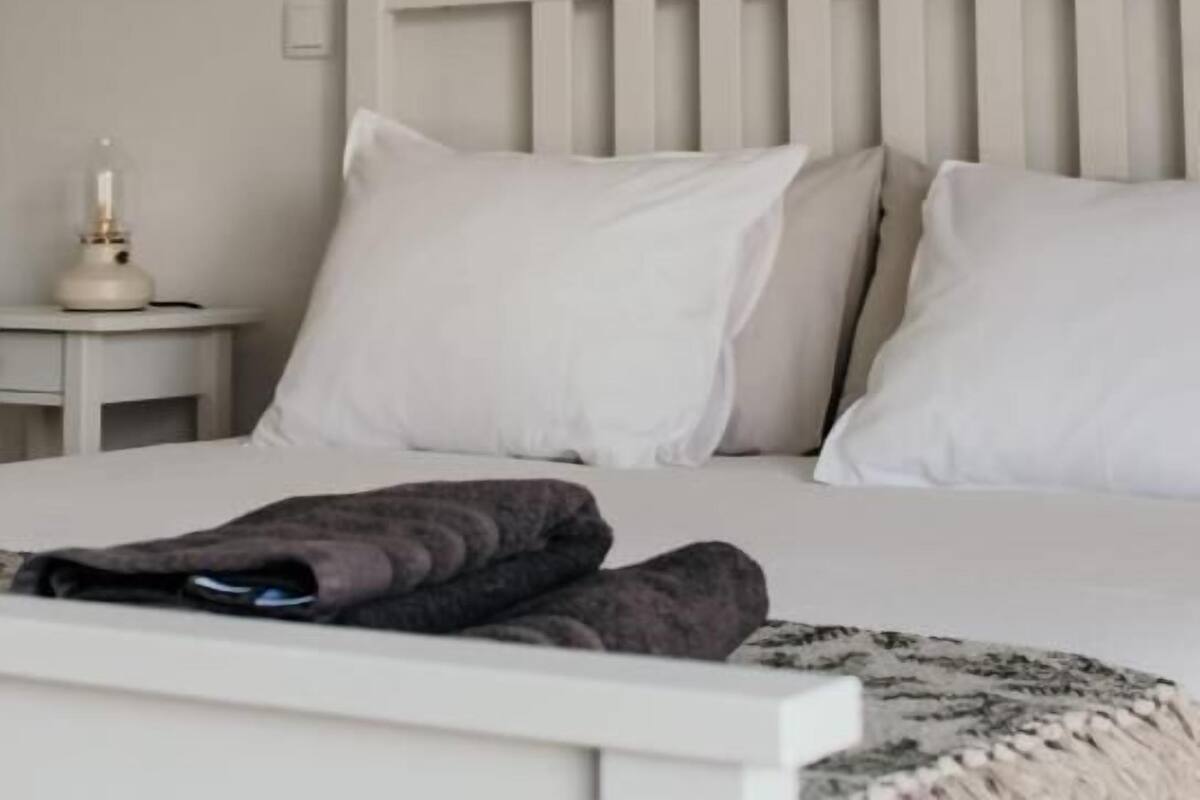 Ein Schlafzimmer mit einem weißen Bett, weißen Kissen und einem Nachttisch mit Lampe.