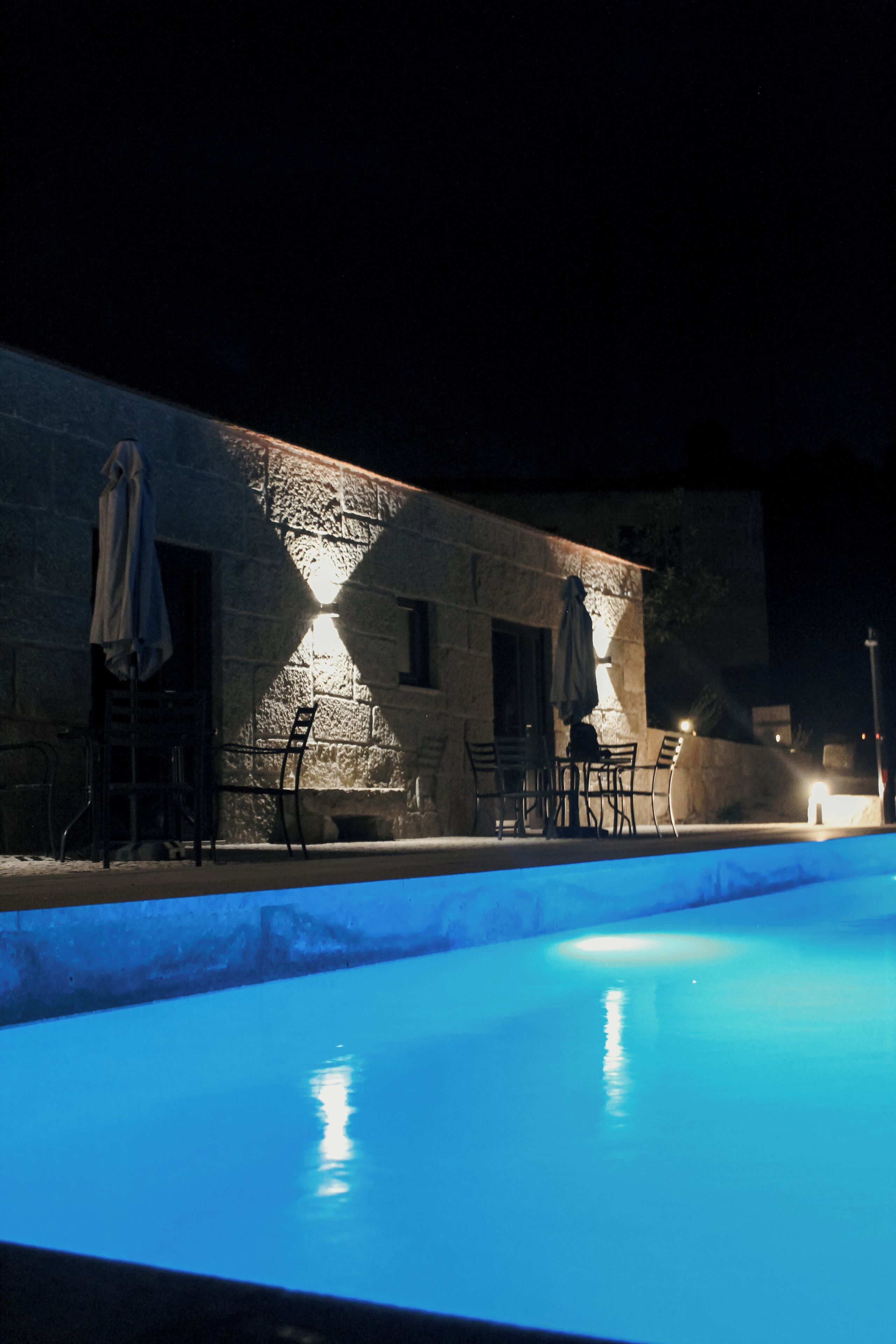 A nighttime swimming pool area with stone walls, outdoor seating, and a well-lit ambiance.