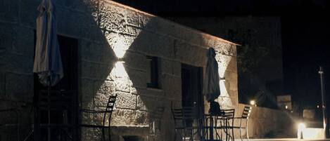 A nighttime swimming pool area with stone walls, outdoor seating, and a well-lit ambiance.