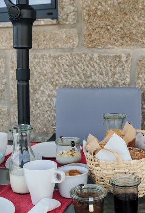 A breakfast setup with a coffee maker, milk jug, coffee cups, jars of spreads, and a basket of bread. - Canhoto Douro (São Lourenço do Douro)
