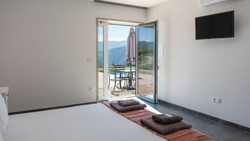 Un dormitorio con cama, televisión y puerta corrediza de vidrio que da a un área de estar exterior con mesa y sillas.