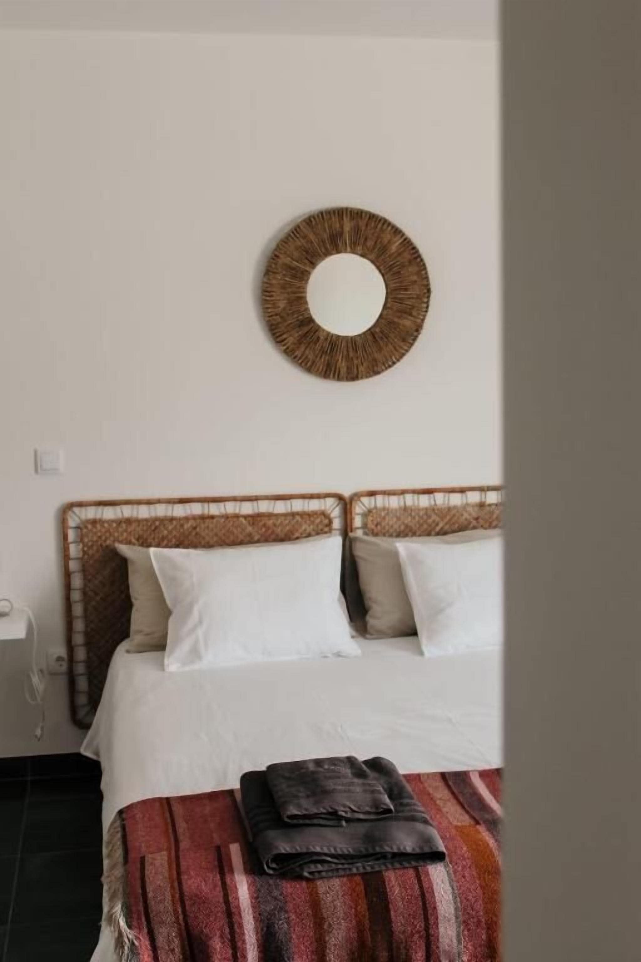 A bed with a woven headboard, white bedding, and a striped blanket.