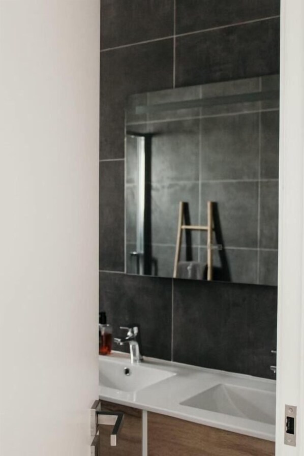 A modern bathroom with a white sink, dark tiled walls, and a wooden ladder leaning against the wall.