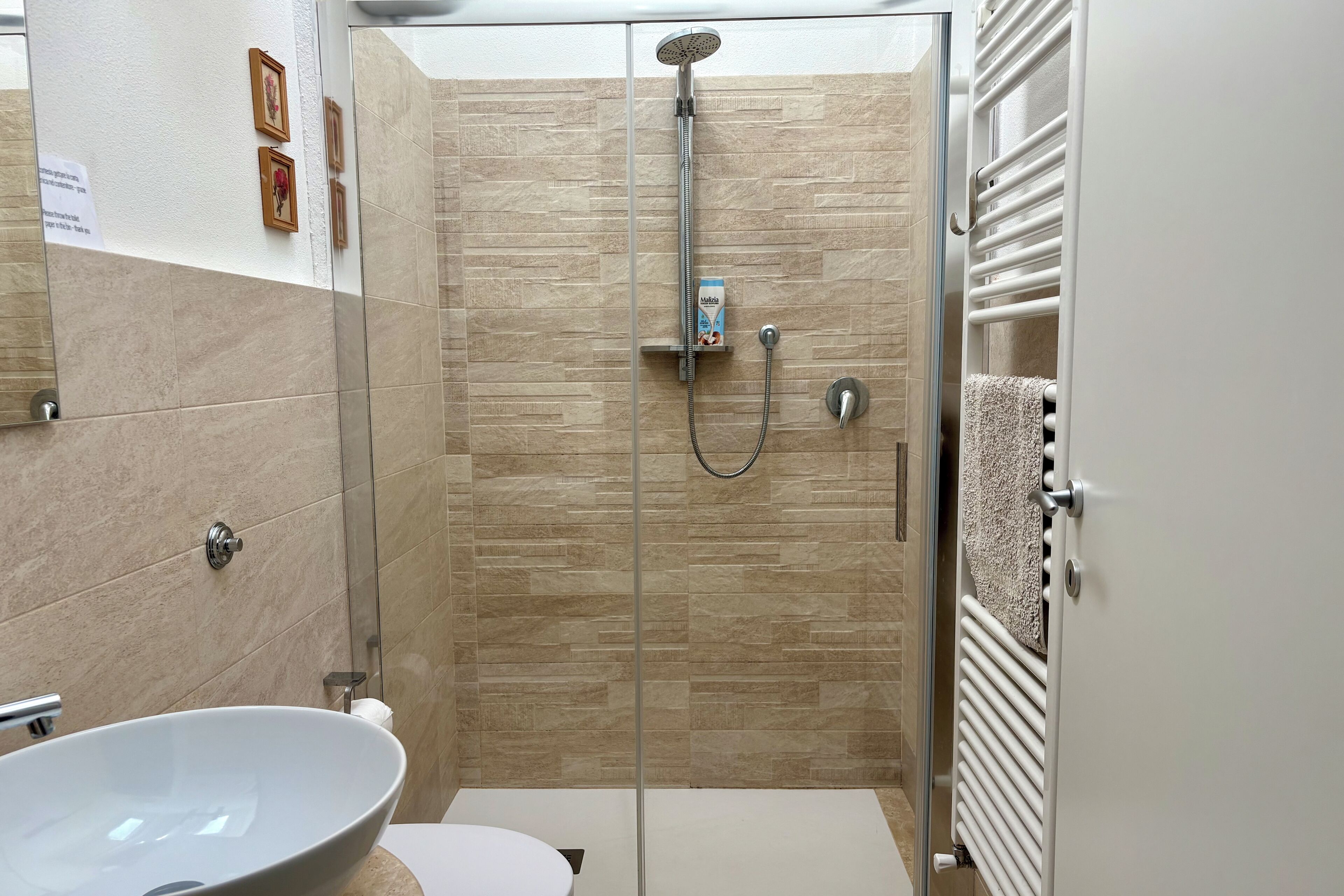 A modern bathroom with a glass shower enclosure, a white sink, and a towel rack.