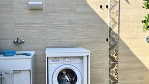 A laundry area with a washing machine and a small cabinet with a sink and a blue basket. - B&B Dimora Orrù (Cabras)