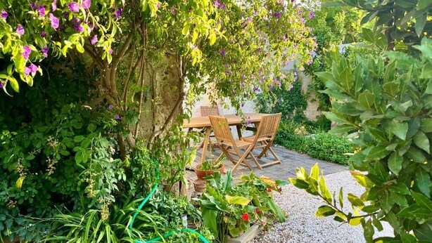An outdoor seating area with a table and chairs surrounded by lush greenery and flowering plants. - B&B Dimora Orrù (Cabras)