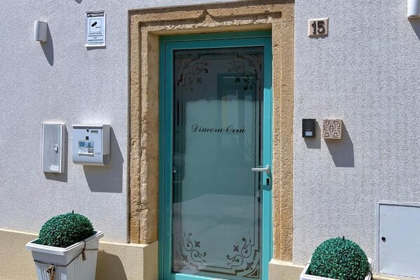 Un bâtiment avec une porte turquoise portant l’inscription « Dimora Città », un petit arbuste vert et le chiffre « 15 » peint sur le mur.