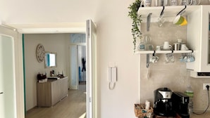 A modern kitchen with a coffee maker, shelves with dishes, and a phone on the wall. - B&B Dimora Orrù (Cabras)