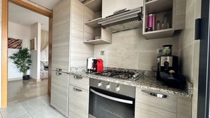 Een moderne keuken met een inbouwfornuis, oven en magnetron. Op het aanrecht staat een koffiezetapparaat, en in de hoek een potplant.