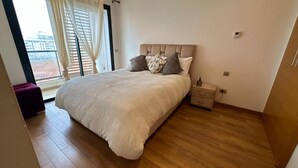 Een slaapkamer met een groot bed, een nachtkastje en een raam met gordijnen.