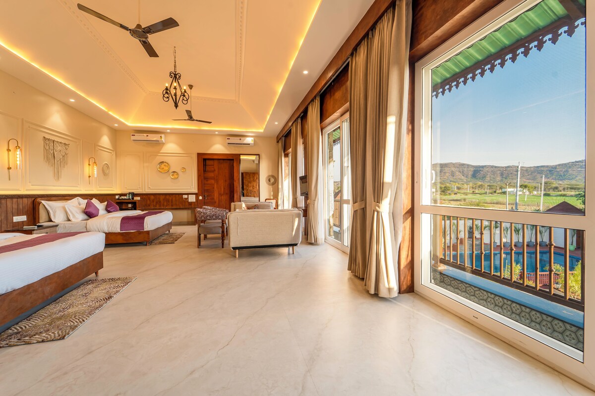 A spacious bedroom with a large bed, a sitting area, and a balcony with a pool view.