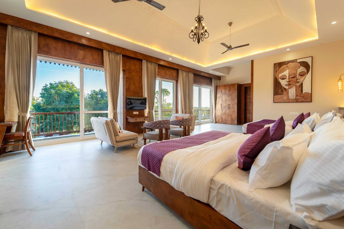 A spacious bedroom with a large bed, a TV, a balcony, and a ceiling fan.