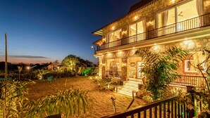 A stone building with a balcony, a staircase leading to the entrance, and a well-lit garden area. - Geeta Bagh - Luxury Private Pool Villa In Pushkar (Riyanbaddi)