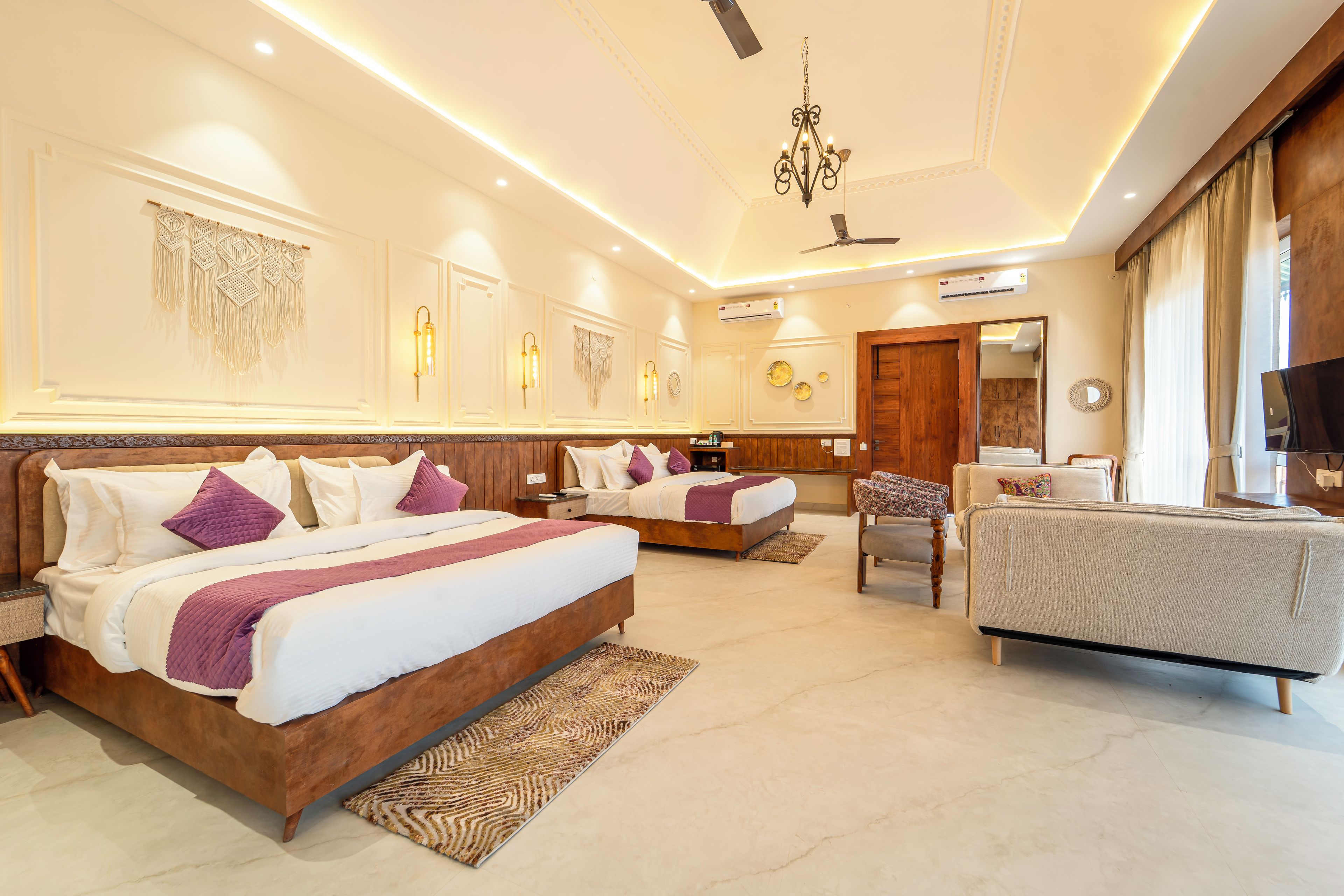 A hotel room with two beds, a sofa, a TV, and a ceiling fan.