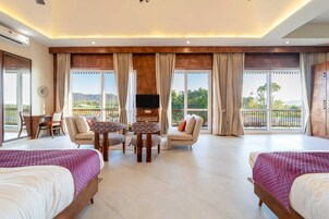 Habitación amplia con dos camas, televisión, mesa de comedor y balcón con vistas a las montañas.