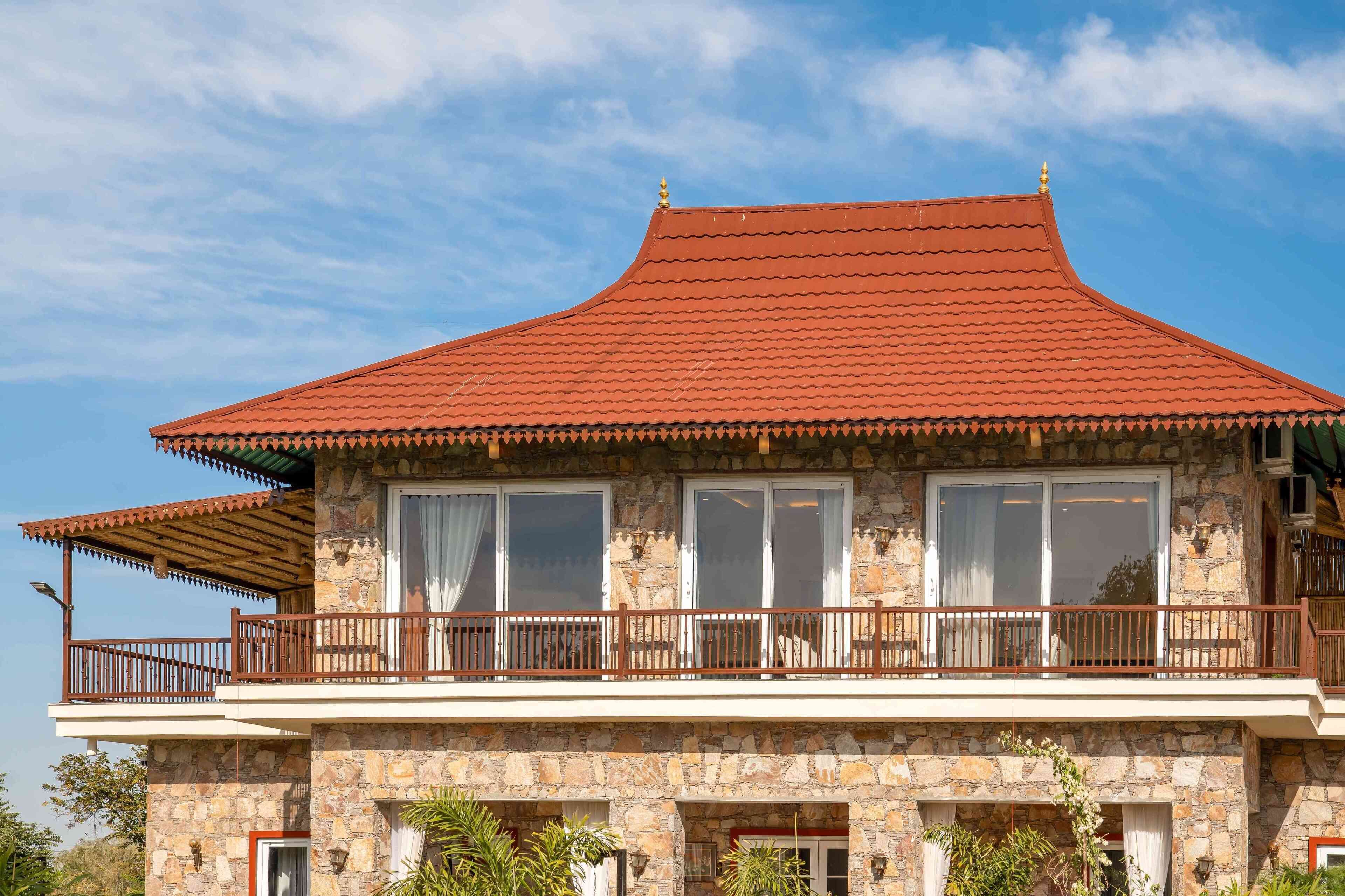 A two-story building with a red-tiled roof, stone facade, and a balcony with a wooden railing.