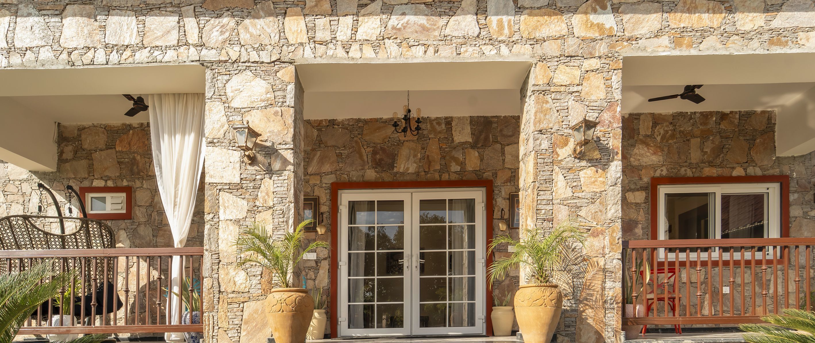 A stone facade with a large glass door, potted plants, and a metal railing.