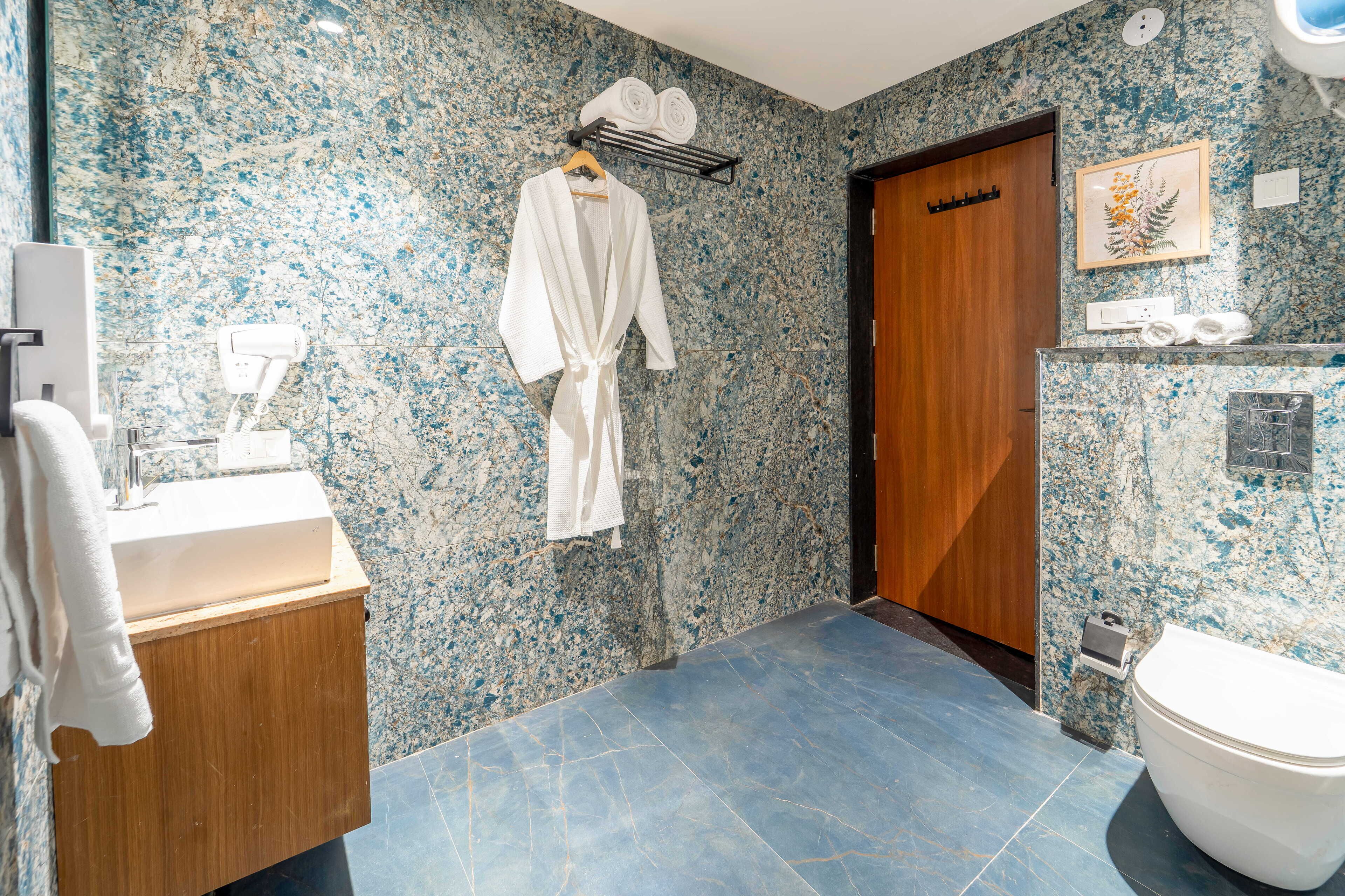A bathroom with a marble backsplash, a wooden vanity, a white bathtub, and a wooden door.