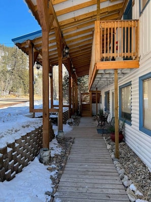 Un pasillo de madera cubierto que lleva a una cabaña con balcón, rodeada de nieve y árboles.