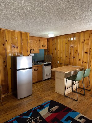 Una cocina compacta con armarios de madera, un refrigerador, una estufa y un pequeño comedor con dos sillas.