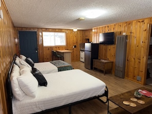 A room with two beds, a desk, a refrigerator, and a television.