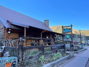 A rustic log cabin with a metal roof, a sign for 'Noble Wines Winery & Grape', and a wooden fence with a 'CAUTION HIGH VOLTAGE' sign. - Room 12 at Bellamy's (Red River)