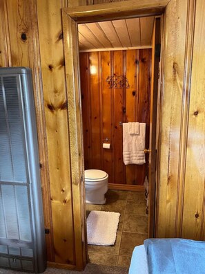 A wooden-paneled bathroom with a toilet, a towel rack, and a shower area. - Room 12 at Bellamy's (Red River)