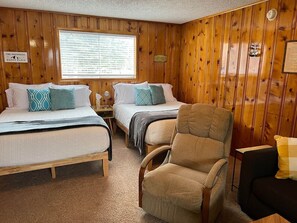 A room with wooden panel walls, two beds with patterned pillows, a chair, and a small table. - Room 12 at Bellamy's (Red River)