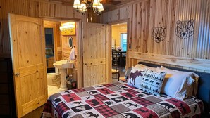 Een kamer met houten lambrisering, een bed, een plafondventilator, een wastafel en een deur naar een andere kamer.