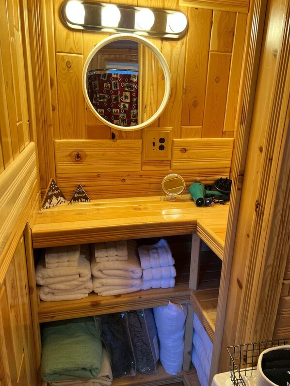 A wooden bathroom vanity with a mirror, lights, and storage for towels and toiletries.