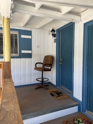 Un banco de madera, una puerta azul y una silla en una habitación con paredes blancas y detalles azules.
