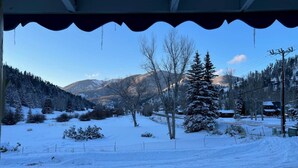 A snowy landscape with a clear view of a mountain range, a few trees, and a building in the distance. - Room 9 at Bellamy's Haus (Red River)
