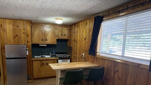 A compact kitchen with wooden cabinets, a refrigerator, a stove, and a bar area with two chairs. - Room 9 at Bellamy's Haus (Red River)