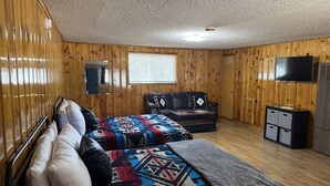A room with wooden walls, a bed with a patterned blanket, a sofa, a television, and a small cabinet. - Room 9 at Bellamy's Haus (Red River)