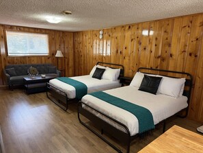 A room with two metal beds, a sofa, a small table, and wooden walls. - Room 10 at Bellamy's (Red River)